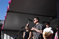Looking up from the side of stage at a small group of delegates speaking on stage. The person speaking is wearing sunglasses and a black and white patterned shirt