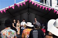 Looking up from the crowd at a small group of delegates speaking on stage. The person speaking is wearing sunglasses and a black and white patterned shirt