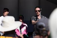 A close shot looking up from the crowd at a small group of delegates speaking on stage. The person speaking is wearing sunglasses and a black and white patterned shirt