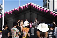 Looking up from the crowd at a small group of delegates speaking on stage. The person speaking is wearing sunglasses and a black and white patterned shirt