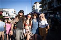 A group of four happy young people stand on a streetscape with a stage seen behind them