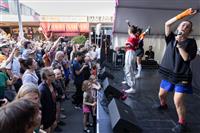 A shot taken from side of stage with three performers waving their hands to a large crowd