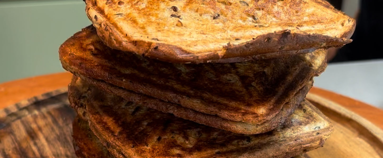 A stack of sealed jaffle-style toasted sandwiches assembled on a chopping board in a kitchen