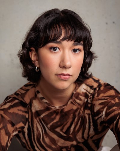 Headshot image of a person with short dark hair with a fringe, wearing a tiger print shirt made of a light material