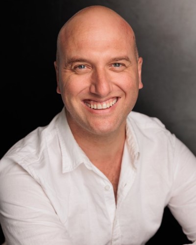 Headshot image of a person with fair skin, shaved head and white collared shirt