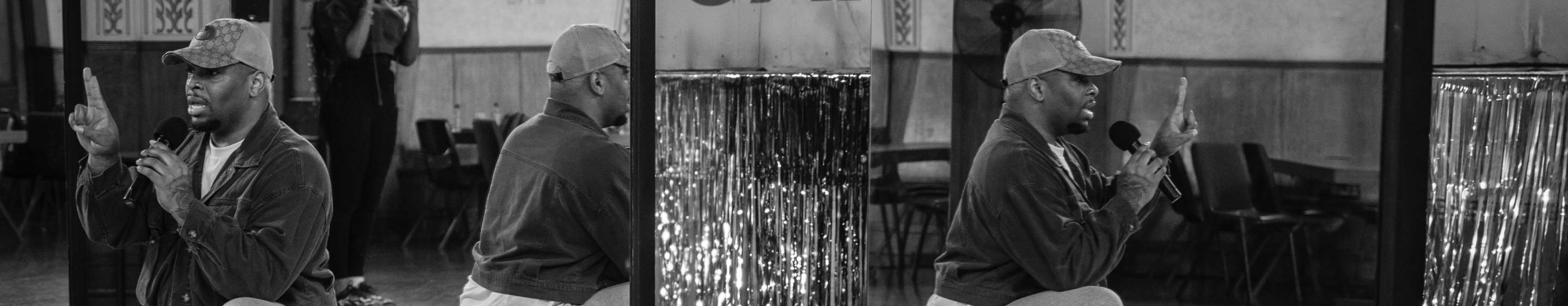 Blakc and white phot of a man in a baseball cap holding a microphone reflected in a miror