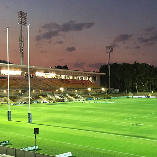 A view of an illuminated rugby league field and grandstand at dusk