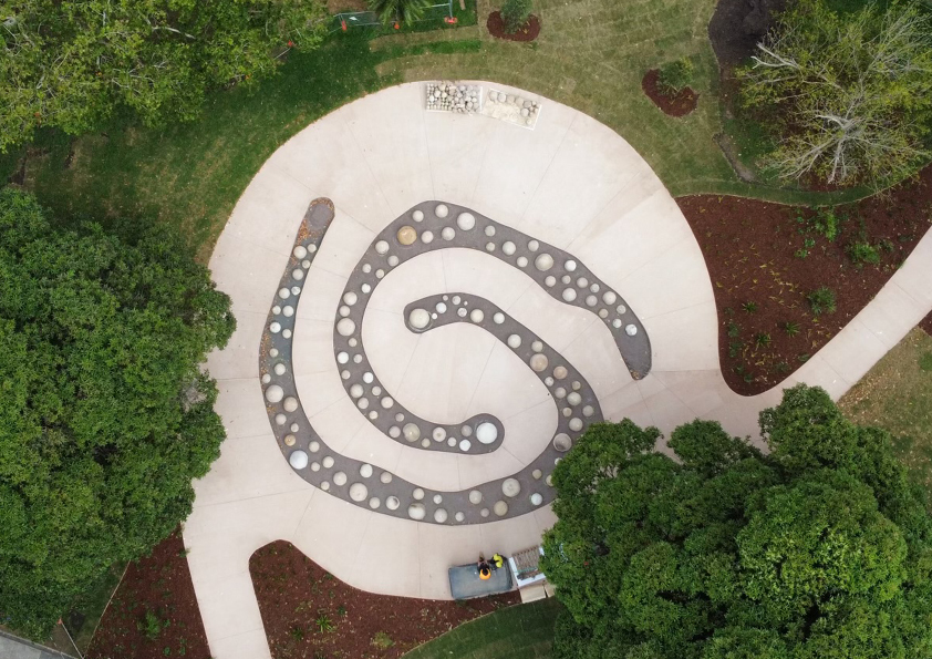 An overhead view of a spiralling outdoor stone artwork set within parklands