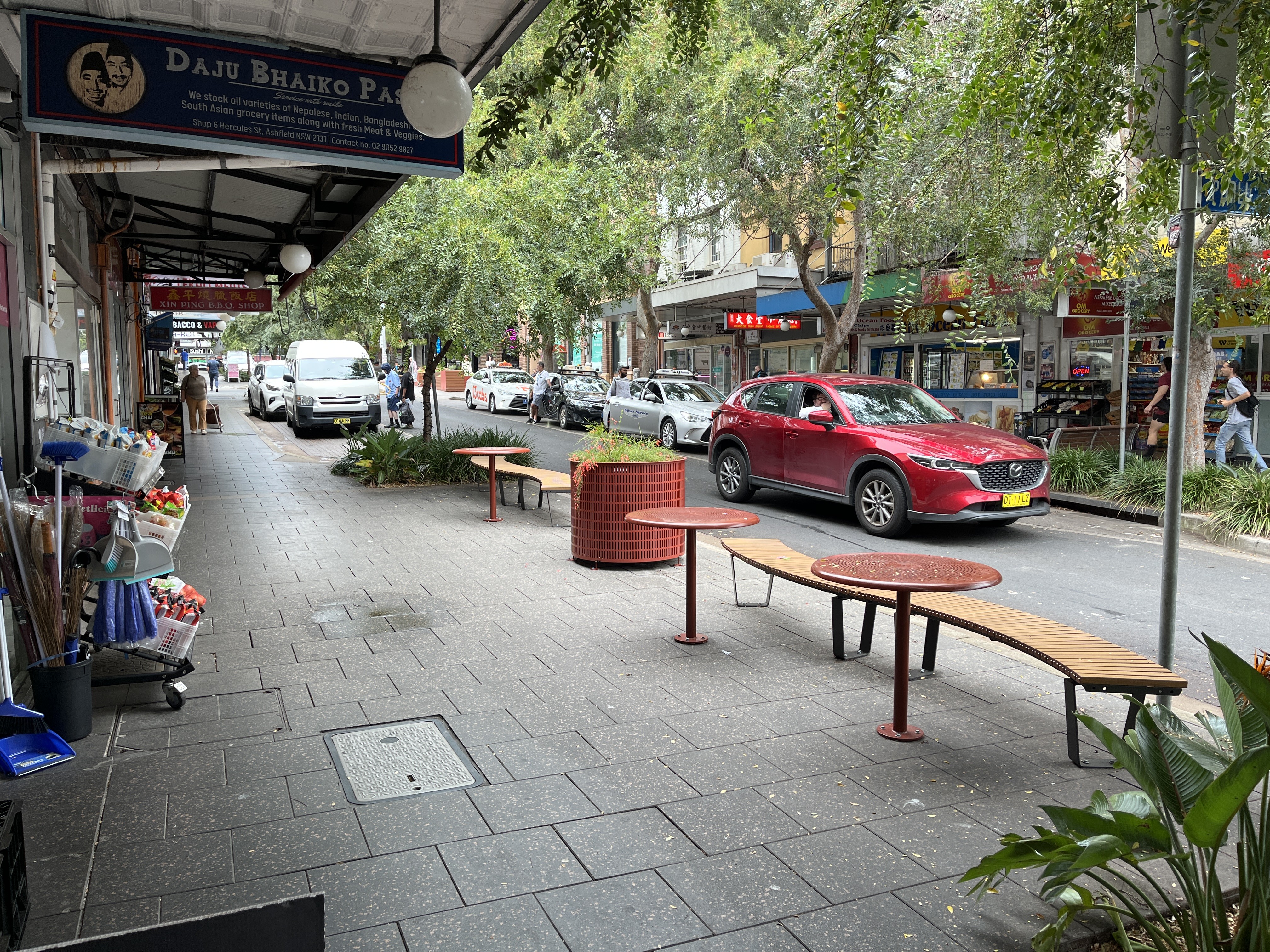 an image of street with outdoor furniture and a red car