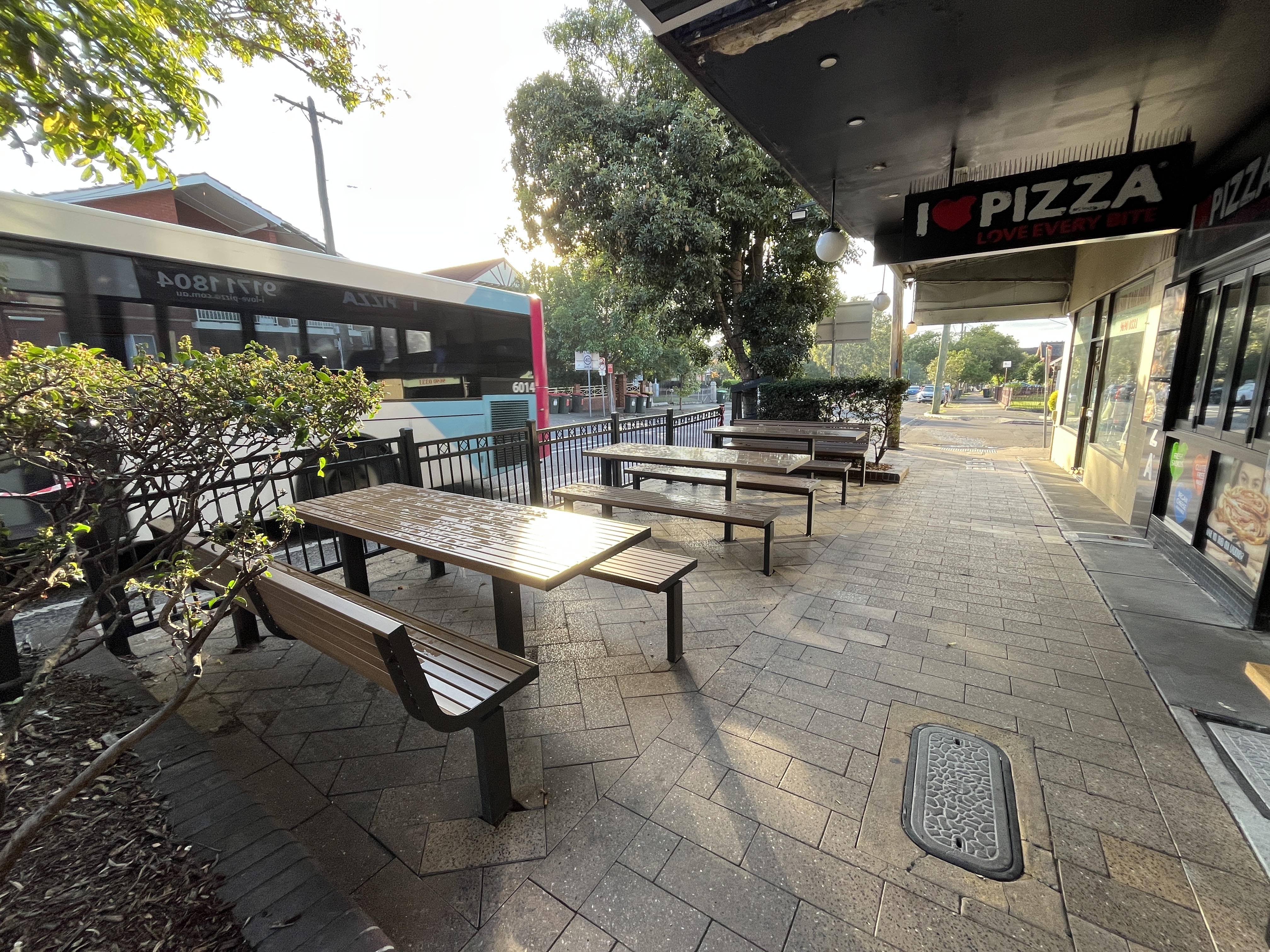 an image of street with outdoor chairs and tables in front of a pizza shop