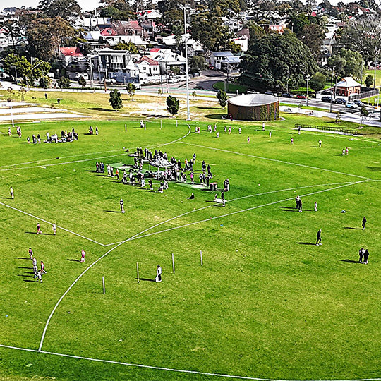  A grass oval sports pitch with Australian rules football markings. Various training activities are taking place on the pitch.