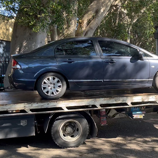 A car on the back of a towtruck in a residential urban street.