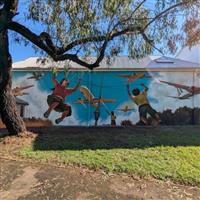 A mural painting of a girl swinging on a hills hoist while an aeroplane flies overhead.
