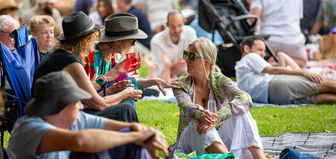 A group of people on picnic chairs and a rug at an outdoor festival.