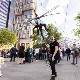 person holds large dragonfly puppet on city street