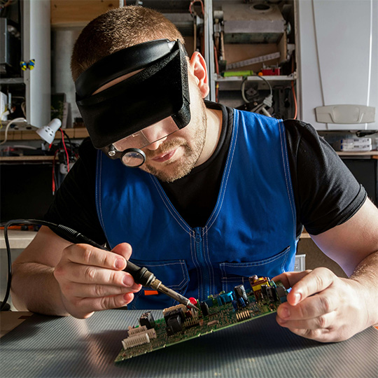 A person holding a soldering iron, repairing an electronics board.