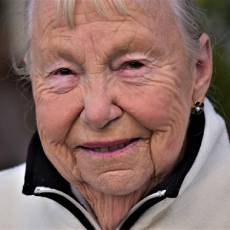 Woman with fair skin and grey hair pulled back wearing a white and black zippered jumper