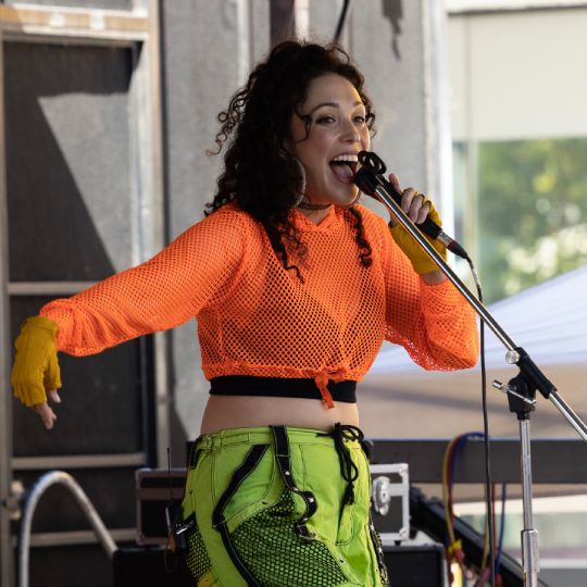 A smiling female singer in bright streetwear performs on stage.