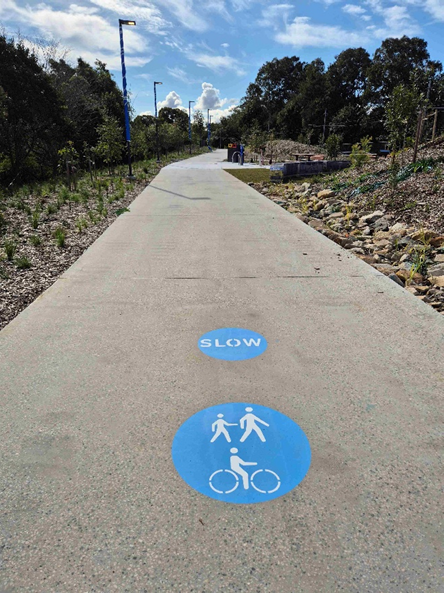 A bike path on the greenway with a slow sign and a shared space sign on the ground.